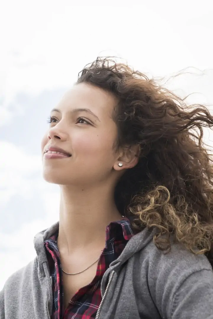 Woman Smiling And Looking Up Against A Cloudy Sky